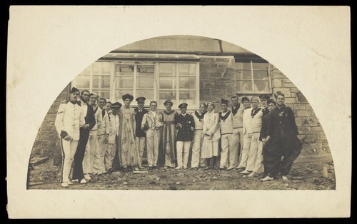 Download the full-sized image of Sailors with men in drag outside a building. Photographic postcard, 191-.