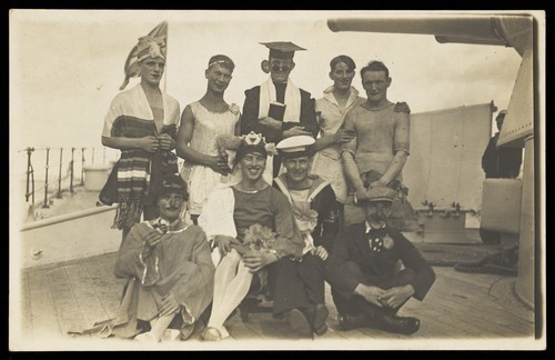 Download the full-sized image of Nine men dressed up on deck. Photographic postcard, 192-.