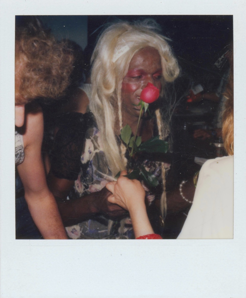 Download the full-sized image of A Photograph of Marsha P. Johnson With Blonde Hair and Red Eyeshadow, Smelling a Rose